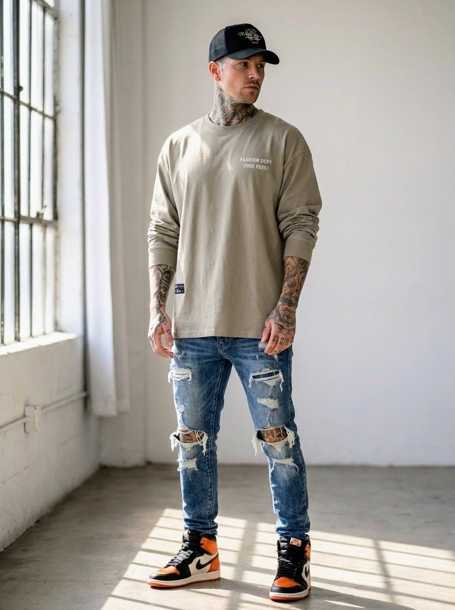 Man wearing oversized beige long sleeve t-shirt, distressed jeans, and sneakers in sunlight
