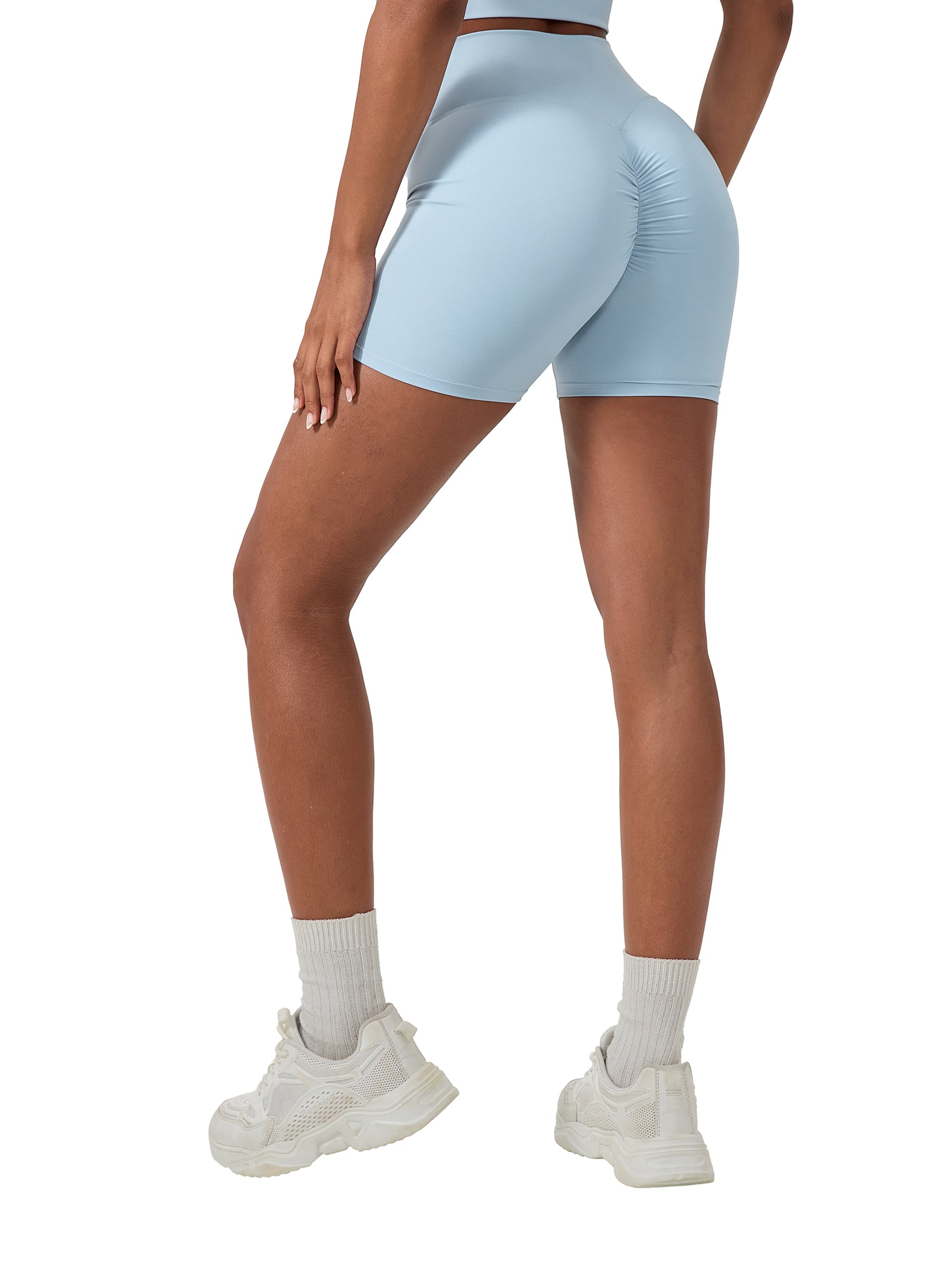 Woman wearing high-waisted light blue biker shorts with ruched seam, white sneakers