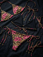 Leopard print string bikini set with pink accents and black fabric details on a dark background