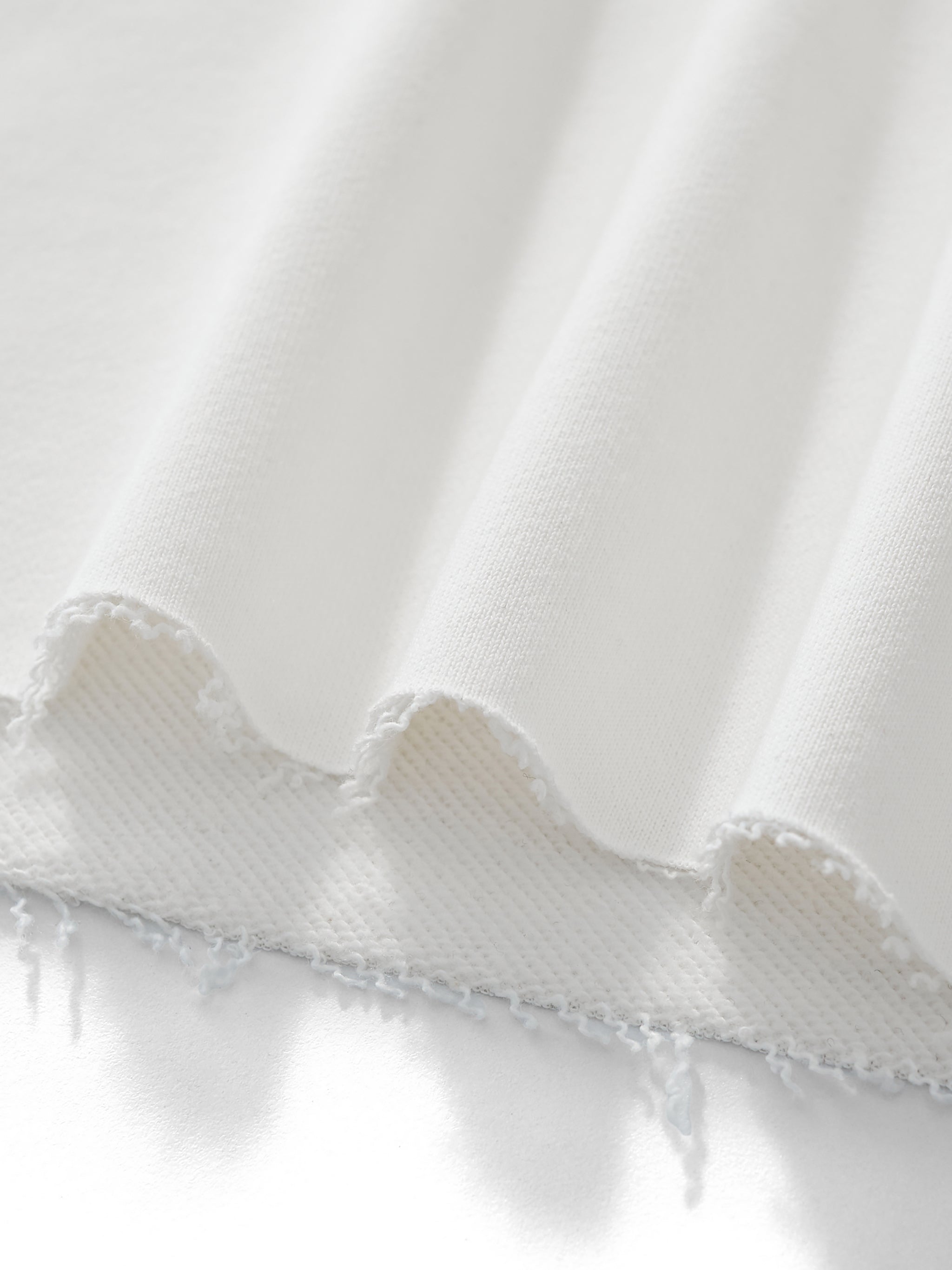Close-up of white heavyweight fabric with raw, frayed hem detail for streetwear