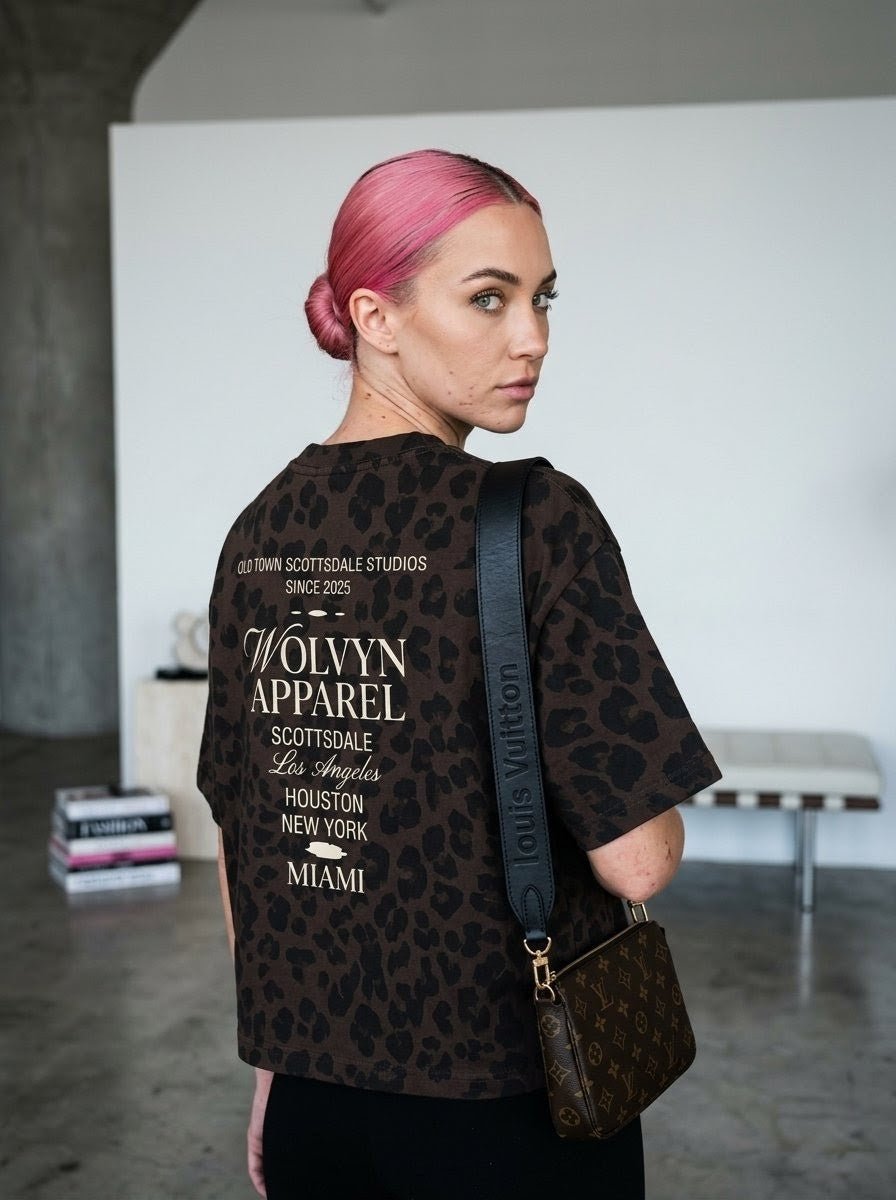 Woman with pink hair wearing a loose, boxy leopard print t-shirt with bold back lettering