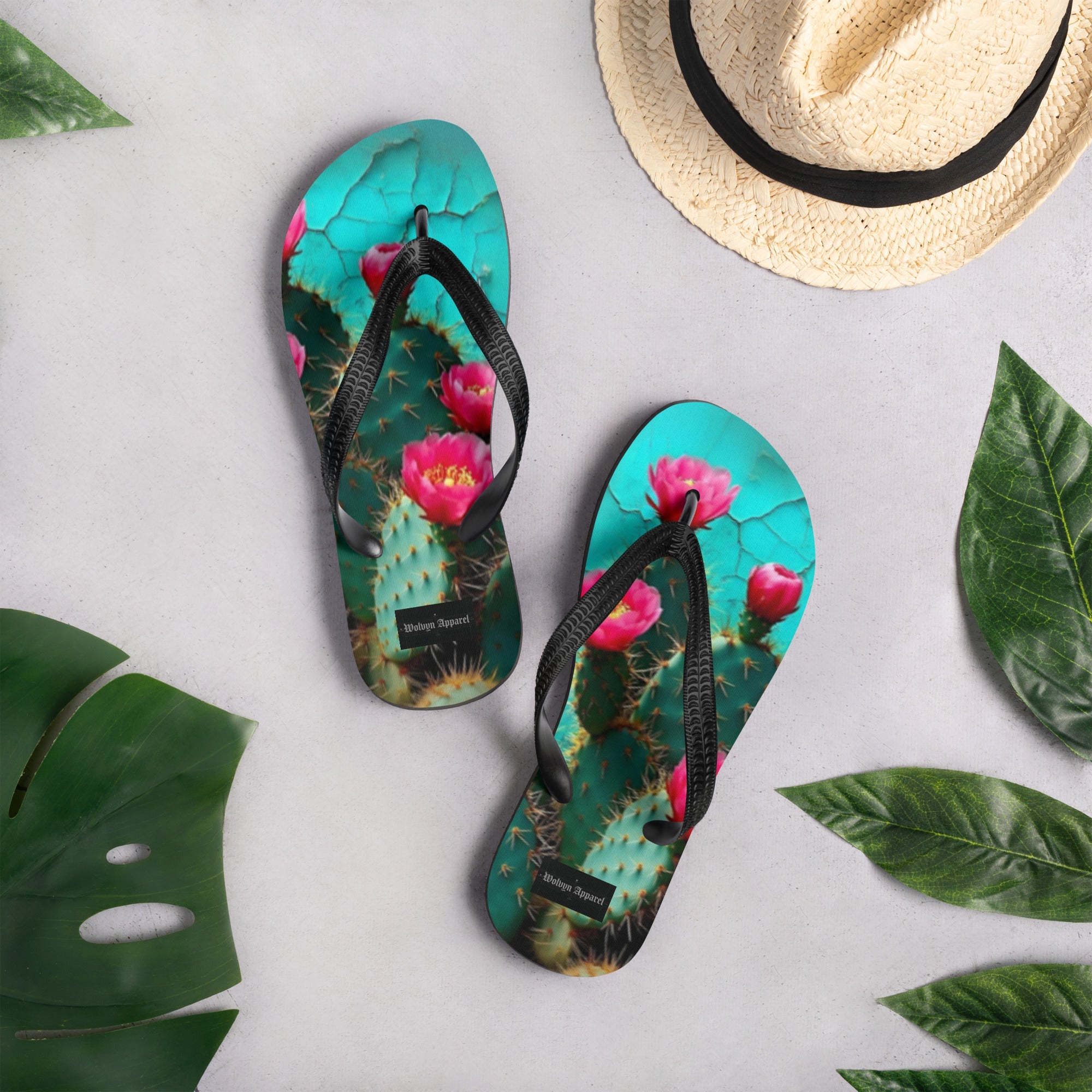 Flip flops with cactus and pink flower design, surrounded by tropical leaves and a straw hat