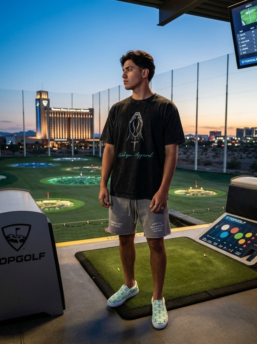 Man in oversized black graphic cotton T-shirt and shorts at Topgolf driving range at sunset