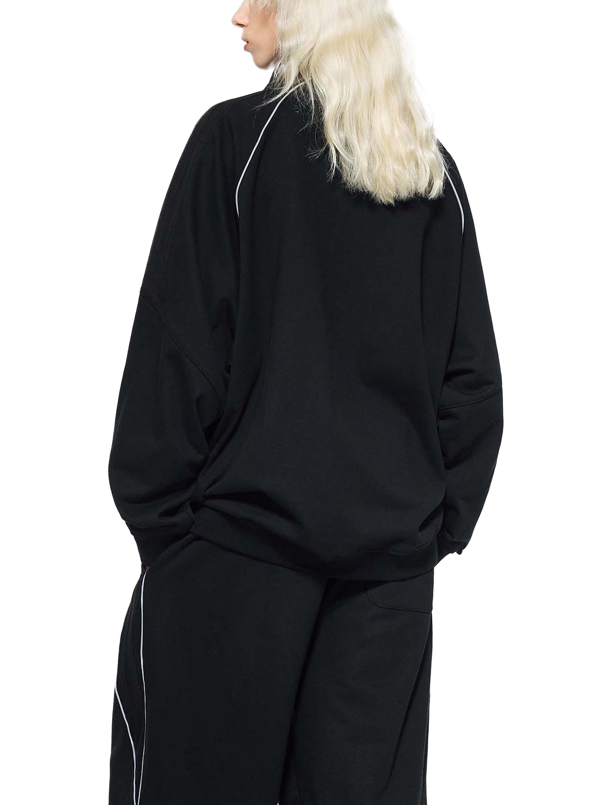 Back view of person wearing black raglan sleeve jacket with white piping details