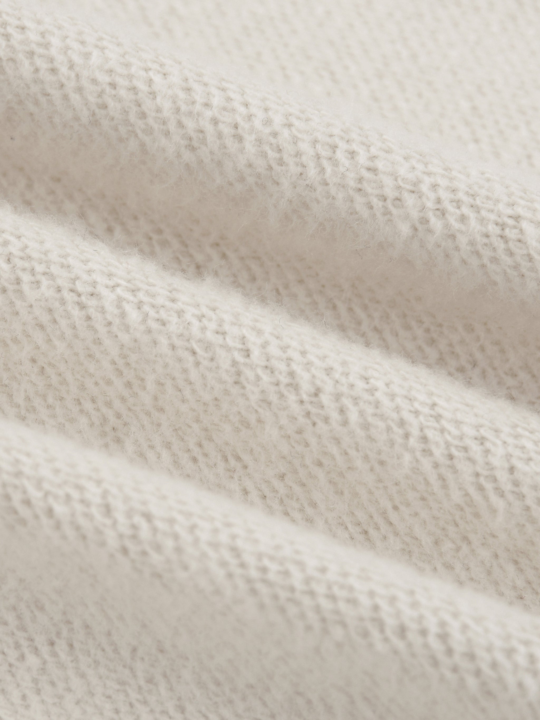 Close-up of heavyweight cream knit fabric with a textured, soft, and ribbed appearance.