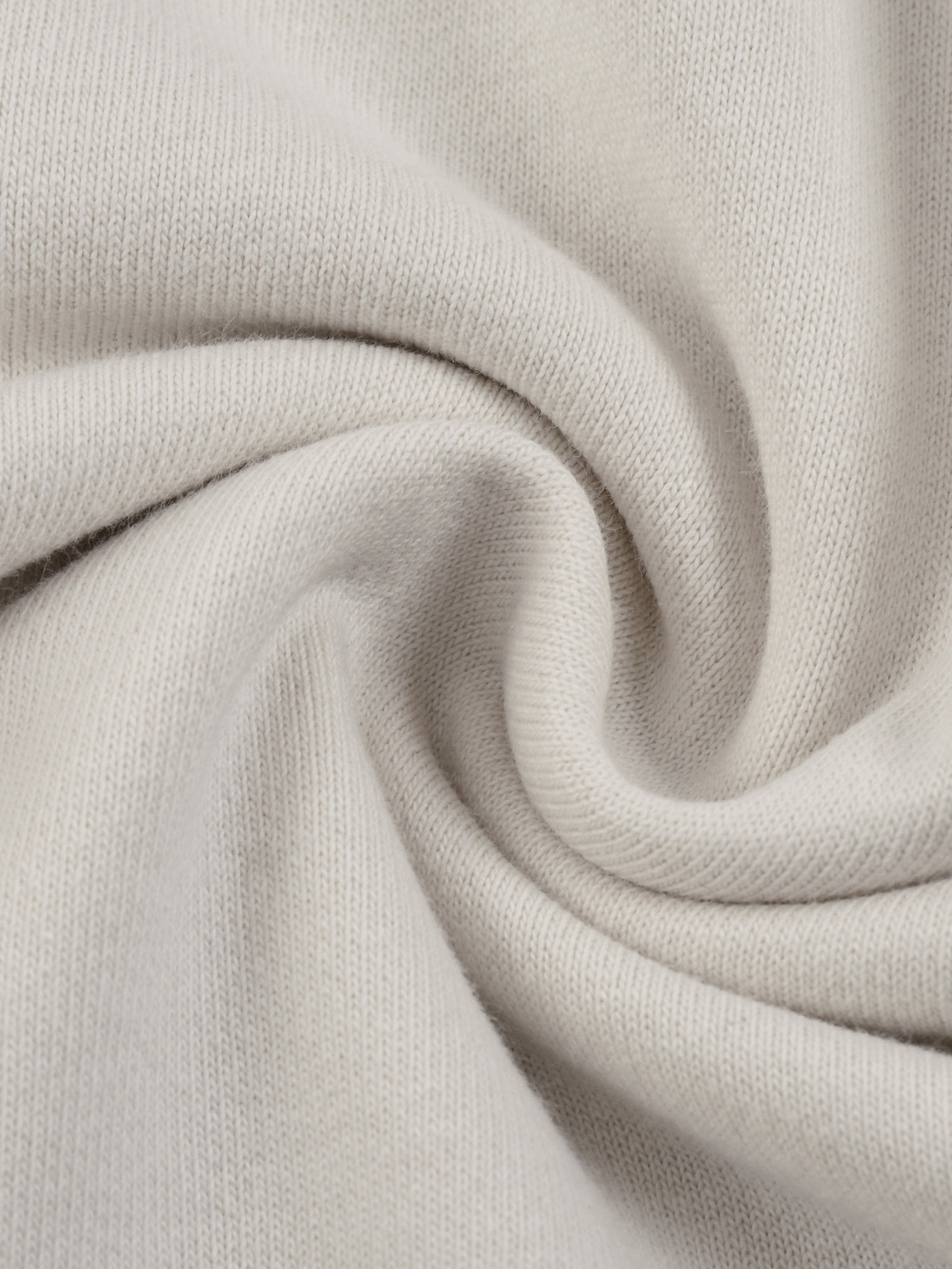 Close-up of soft, heavyweight cream knit fabric with subtle texture and swirl pattern