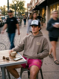Man in a Scottsdale cactus foam trucker hat and casual streetwear sitting at an outdoor café table