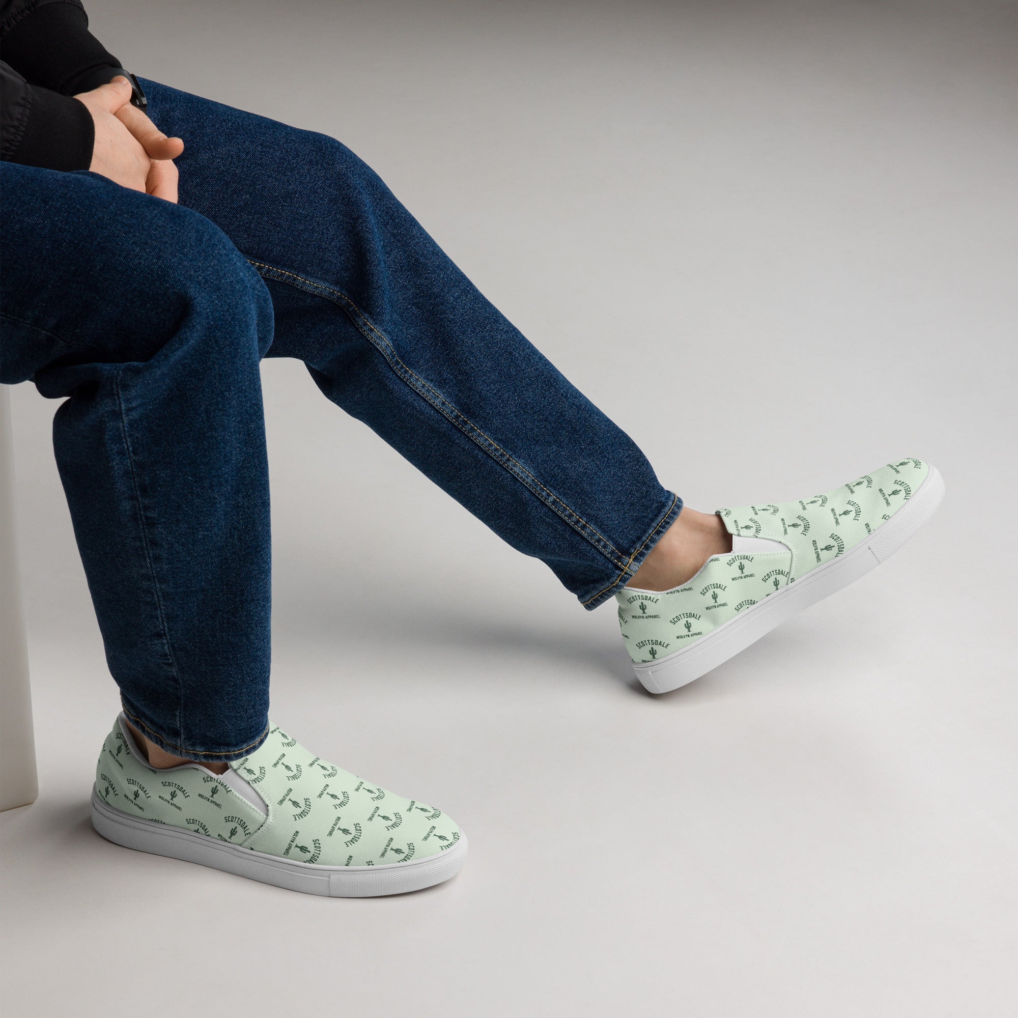 Men's light green slip-on canvas shoes with palm tree print, paired with blue jeans