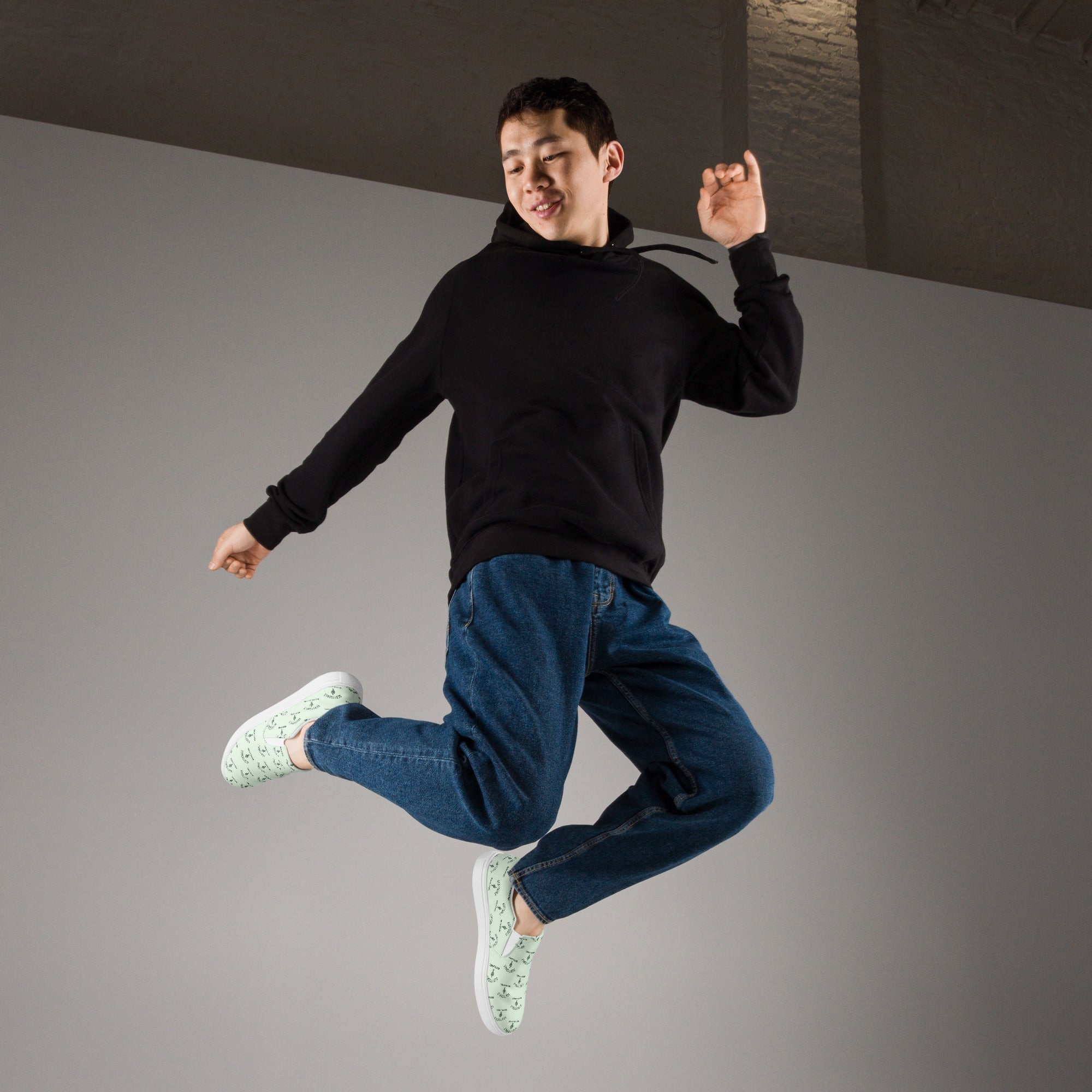 Man jumping in casual streetwear, wearing black hoodie, blue jeans, and slip-on canvas shoes