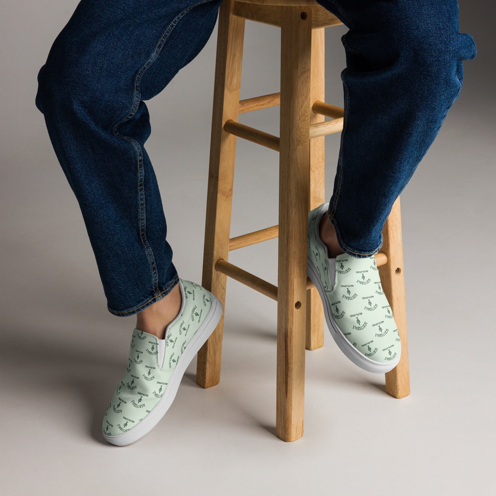 Man wearing mint green slip-on canvas shoes with subtle graphic print, seated on stool