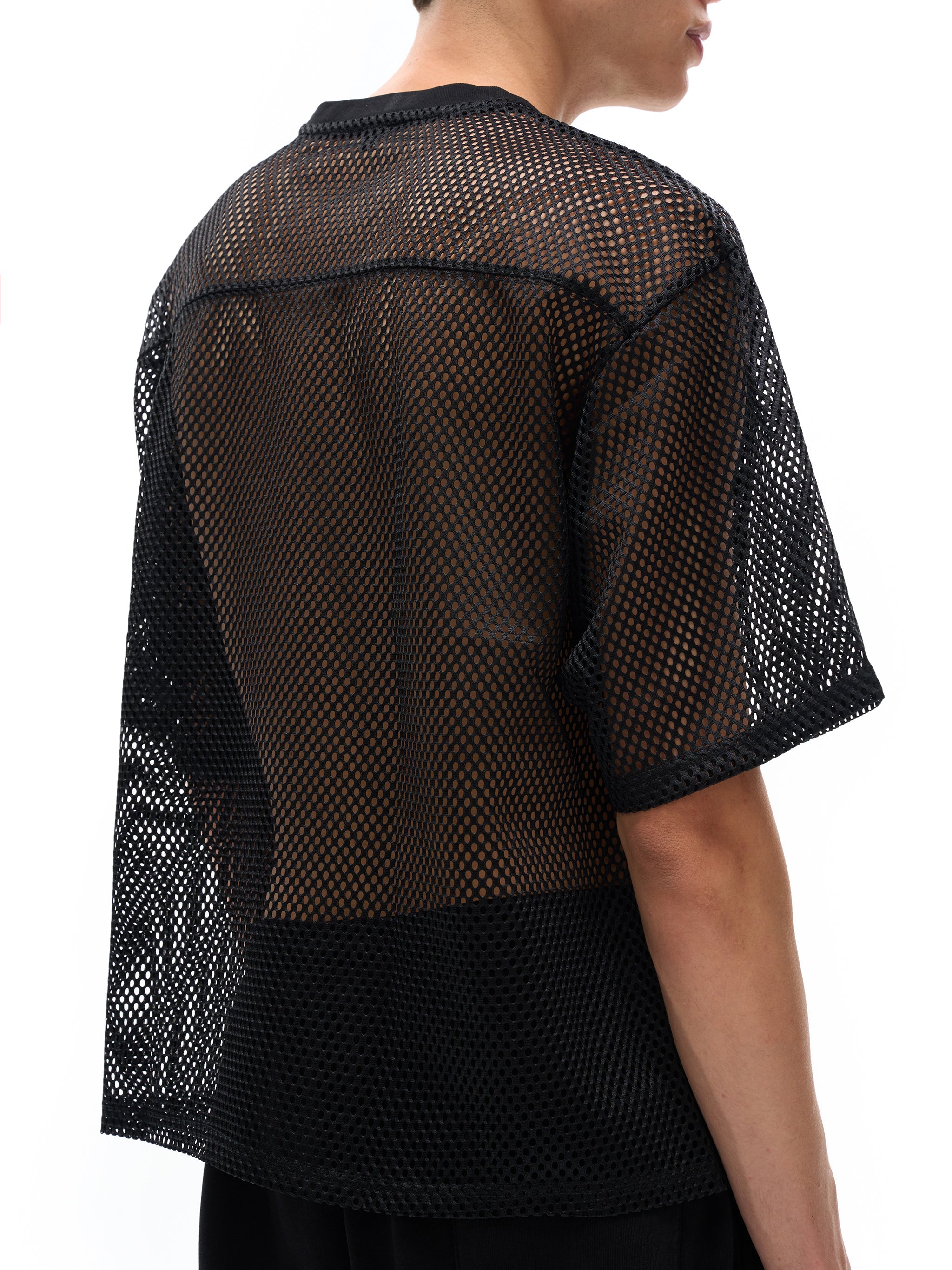 Back view of a model wearing a black see-through boxy net t-shirt with short sleeves
