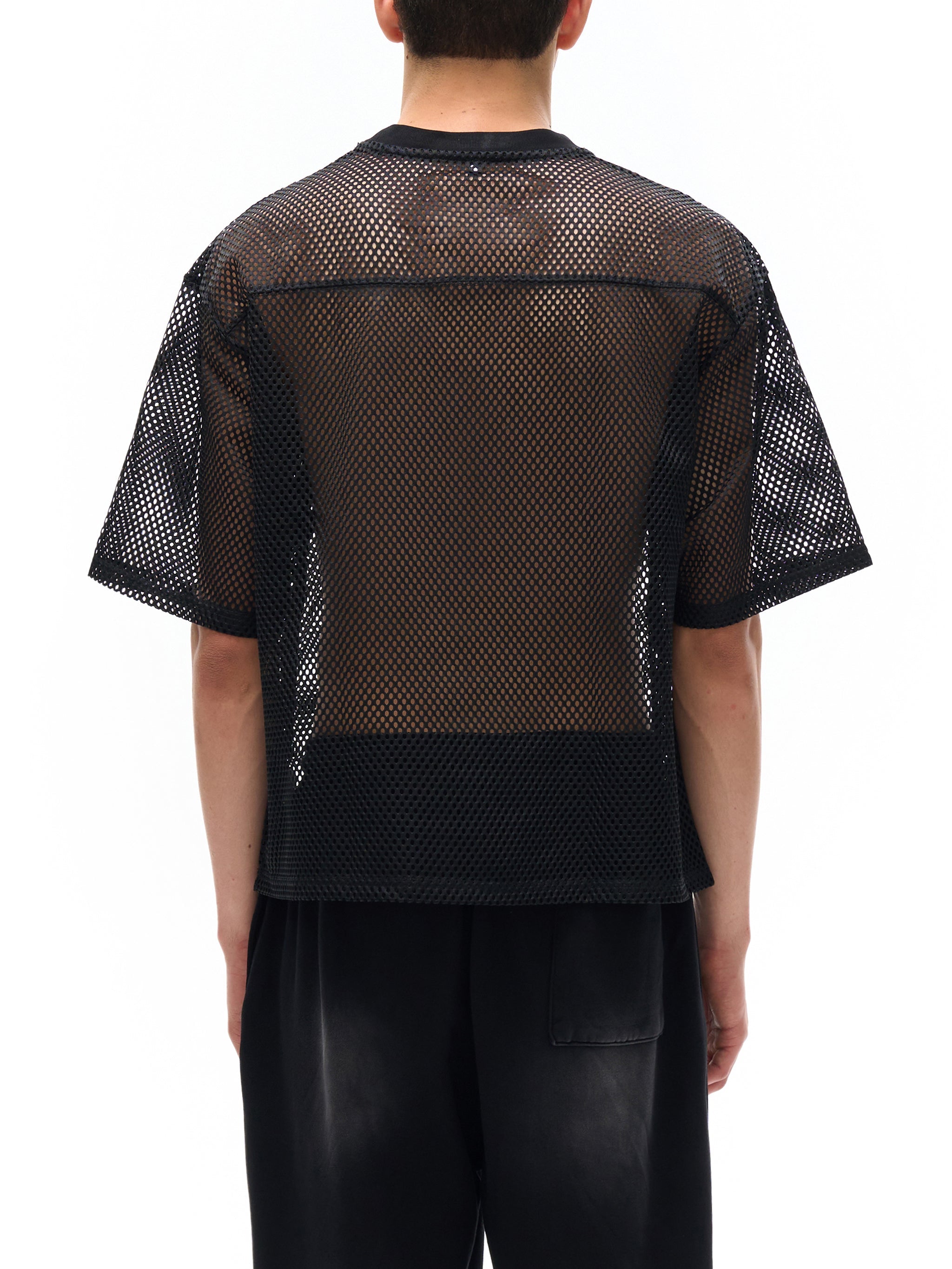 Back view of a boxy black mesh net t-shirt with short sleeves, worn by a male model