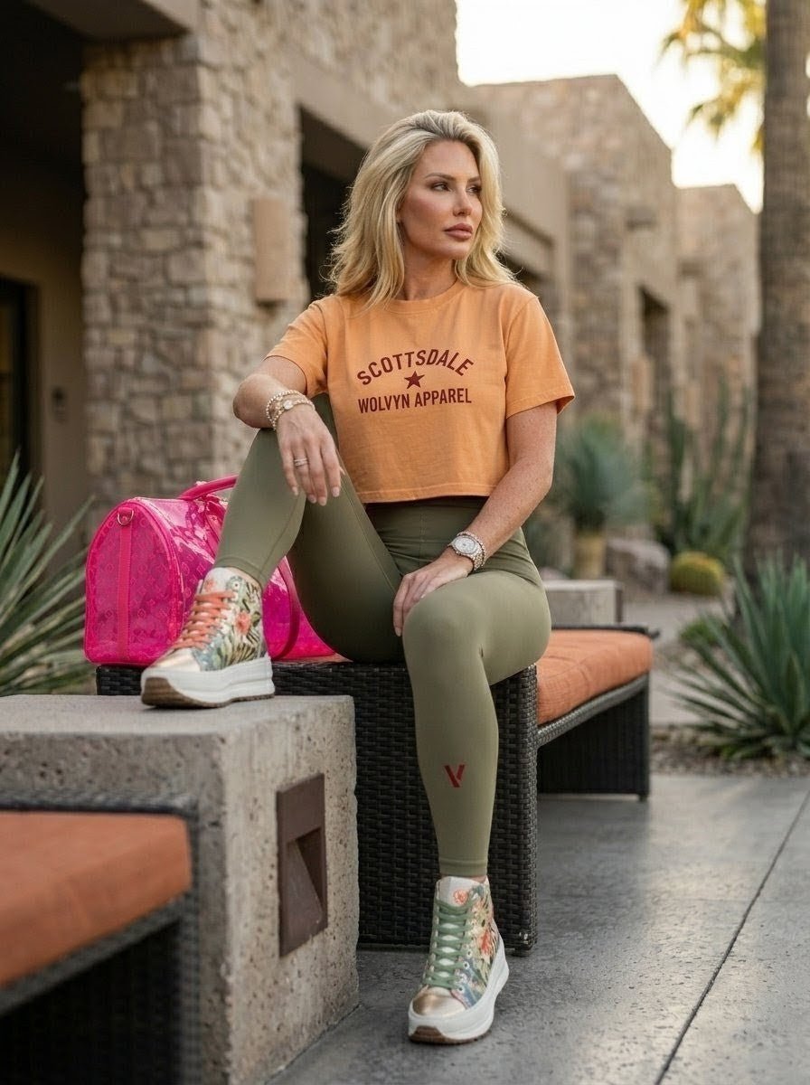 Woman in orange Scottsdale crop top and olive leggings sitting outdoors with pink bag