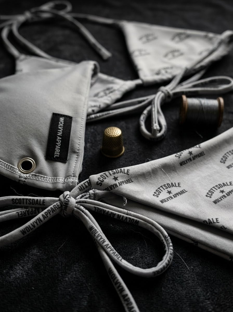 Gray Scottsdale string bikini set with logo print, sewing accessories, close-up on black fabric.