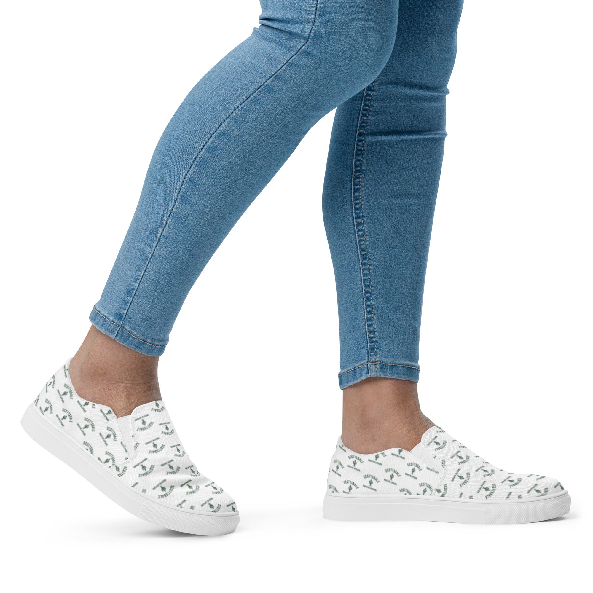Woman wearing white slip-on canvas shoes with green pattern and light blue skinny jeans