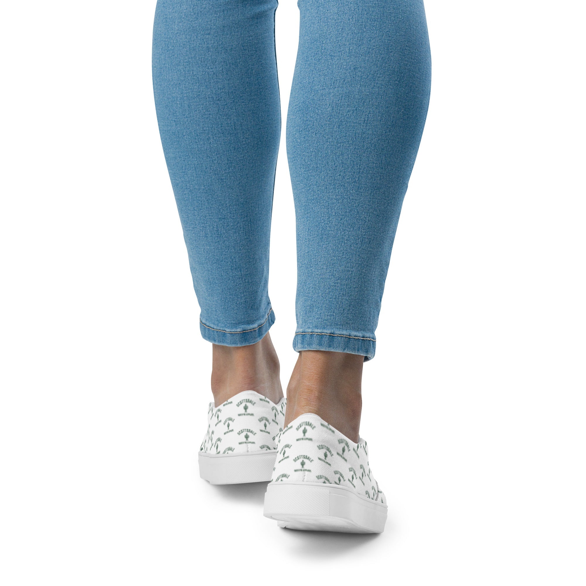 Woman wearing light denim jeans and white slip-on canvas shoes with green palm tree print