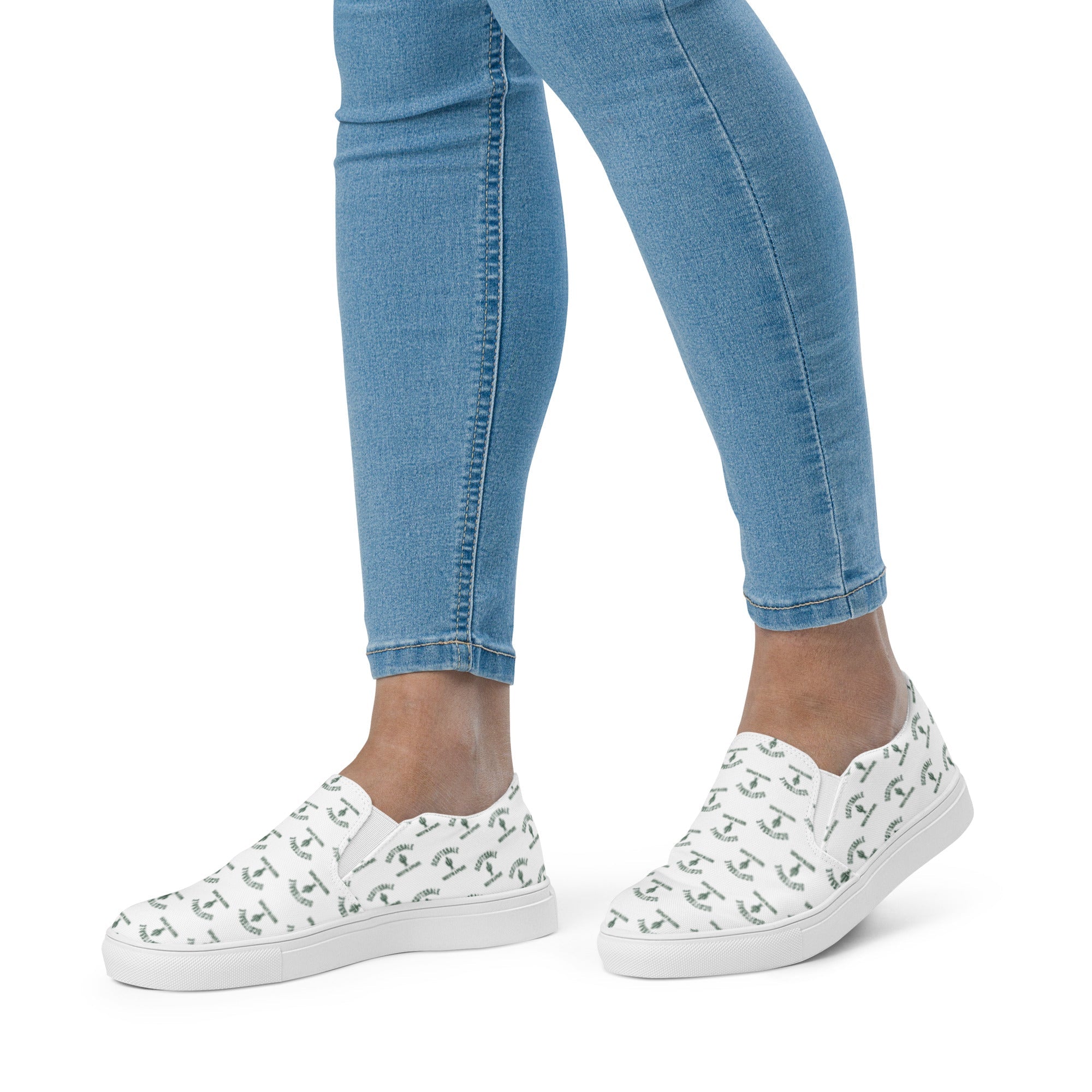 Woman wearing white slip-on canvas shoes with green pattern, paired with light blue skinny jeans