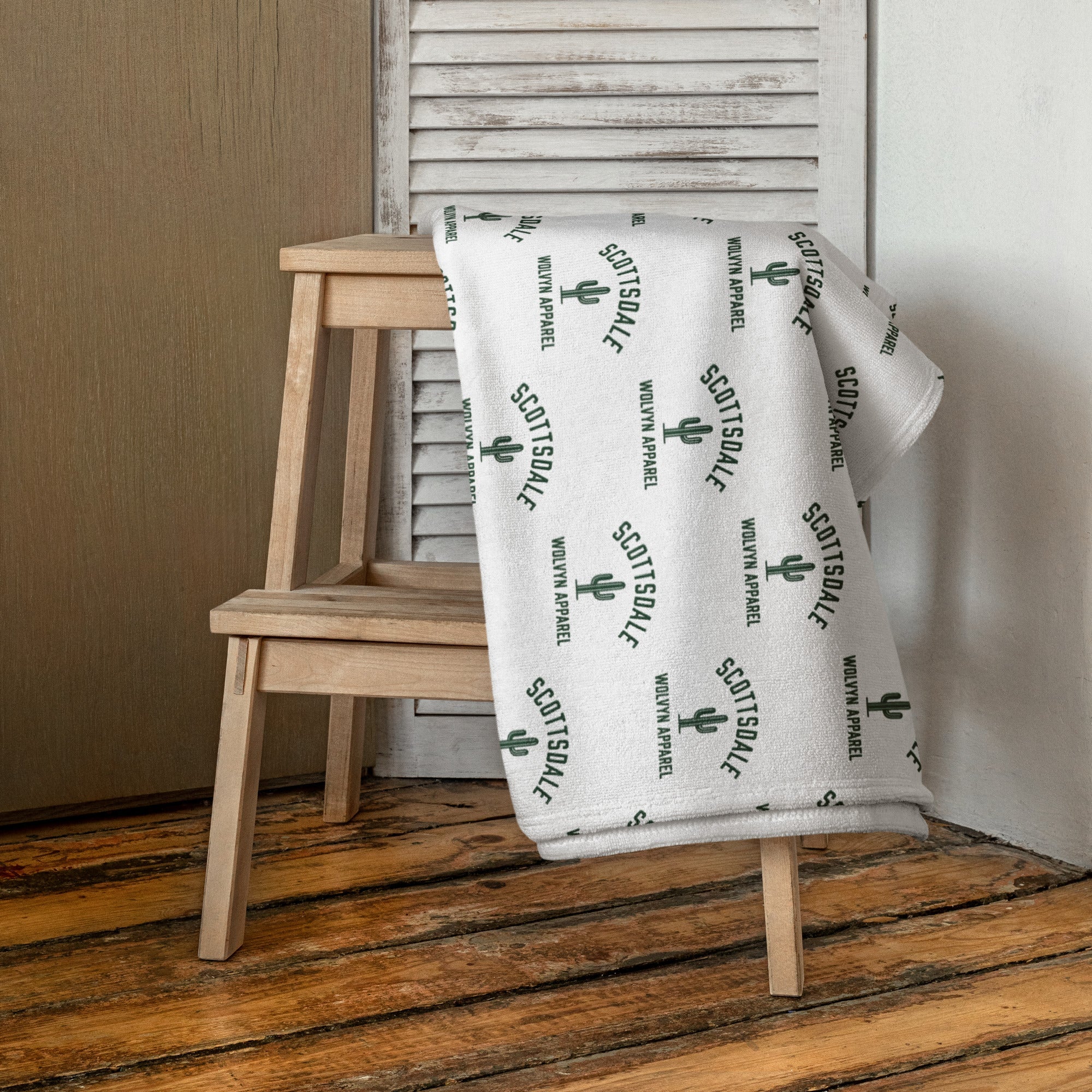 White Scottsdale towel with green cactus print draped over a wooden chair on hardwood floor
