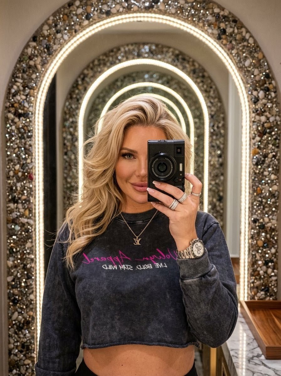 Woman taking mirror selfie in snow washed raw edge cropped sweatshirt with neon lettering, arched mirror background