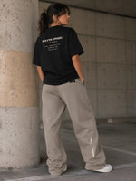 Woman in oversized black t-shirt and beige sweatpants, concrete urban setting, streetwear fashion