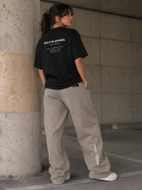 Woman in oversized black t-shirt and beige sweatpants, concrete urban setting, streetwear fashion