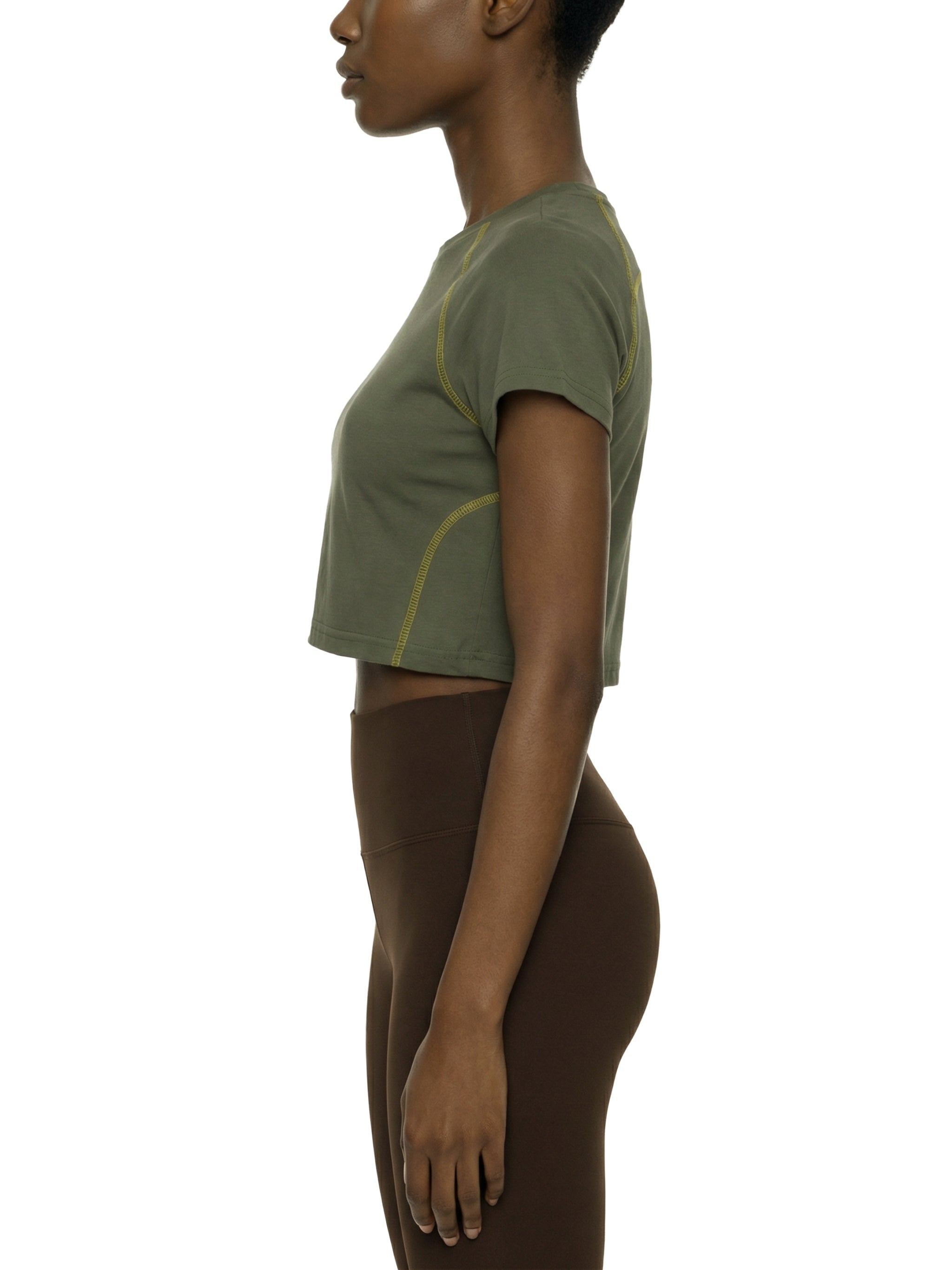 Woman in olive green contrast stitch raglan crop t-shirt and brown leggings, side view