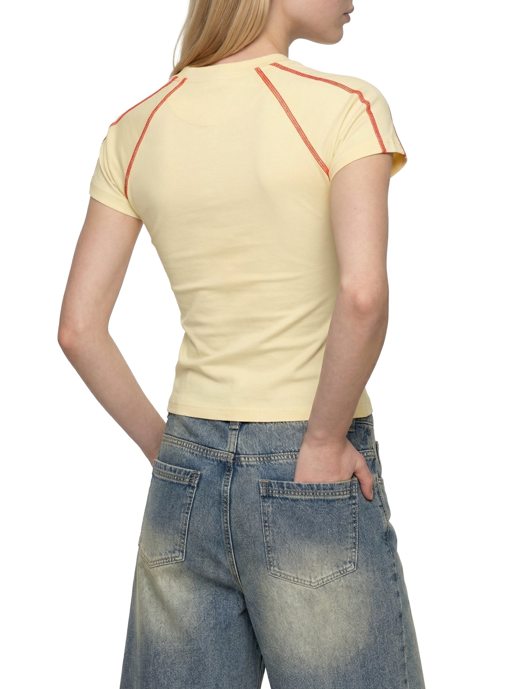 Woman in light yellow contrast stitch raglan t-shirt and faded wide-leg jeans, rear view