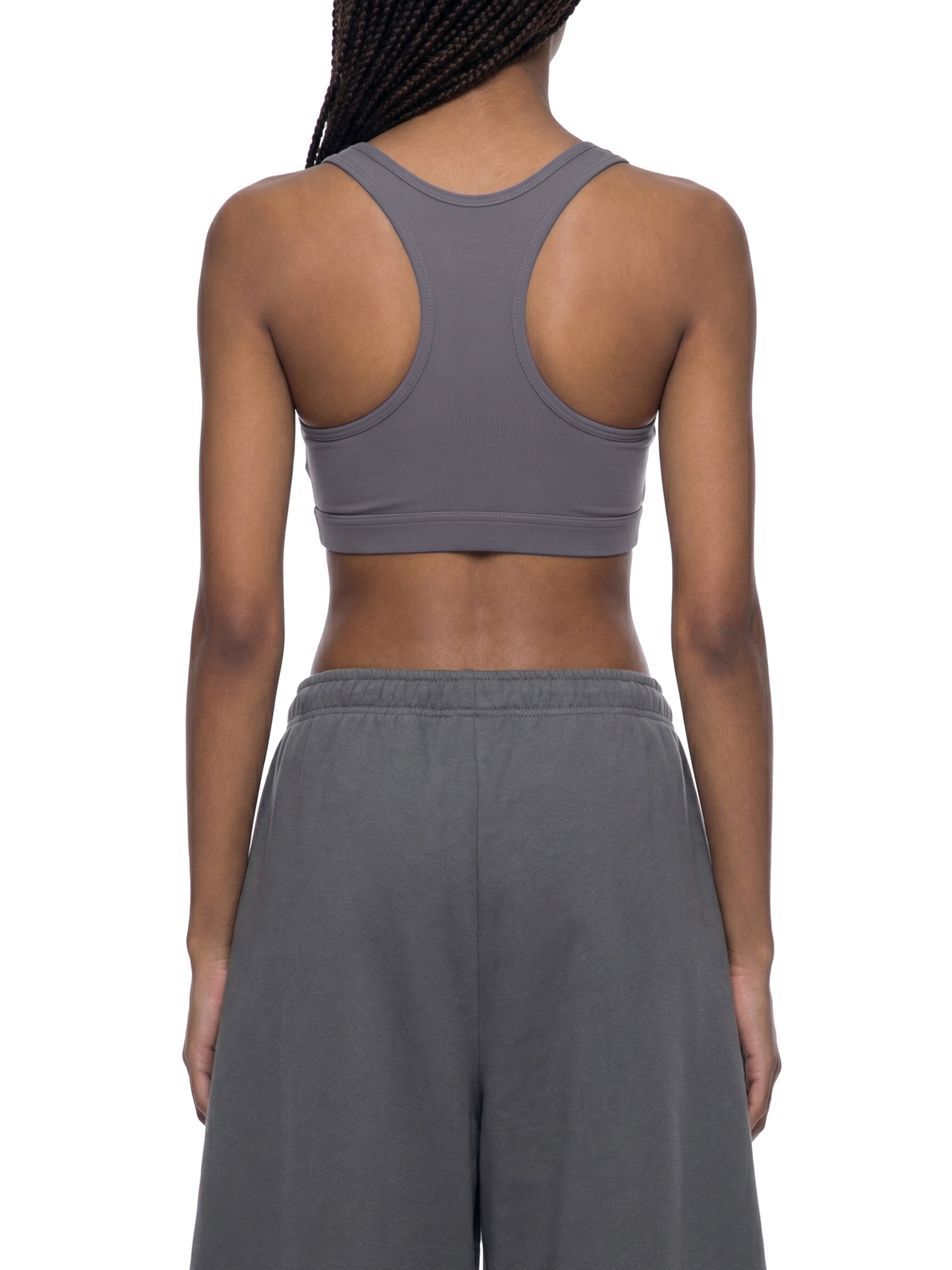 Woman wearing gray cropped sports bra and sweatpants, shown from the back, on white background