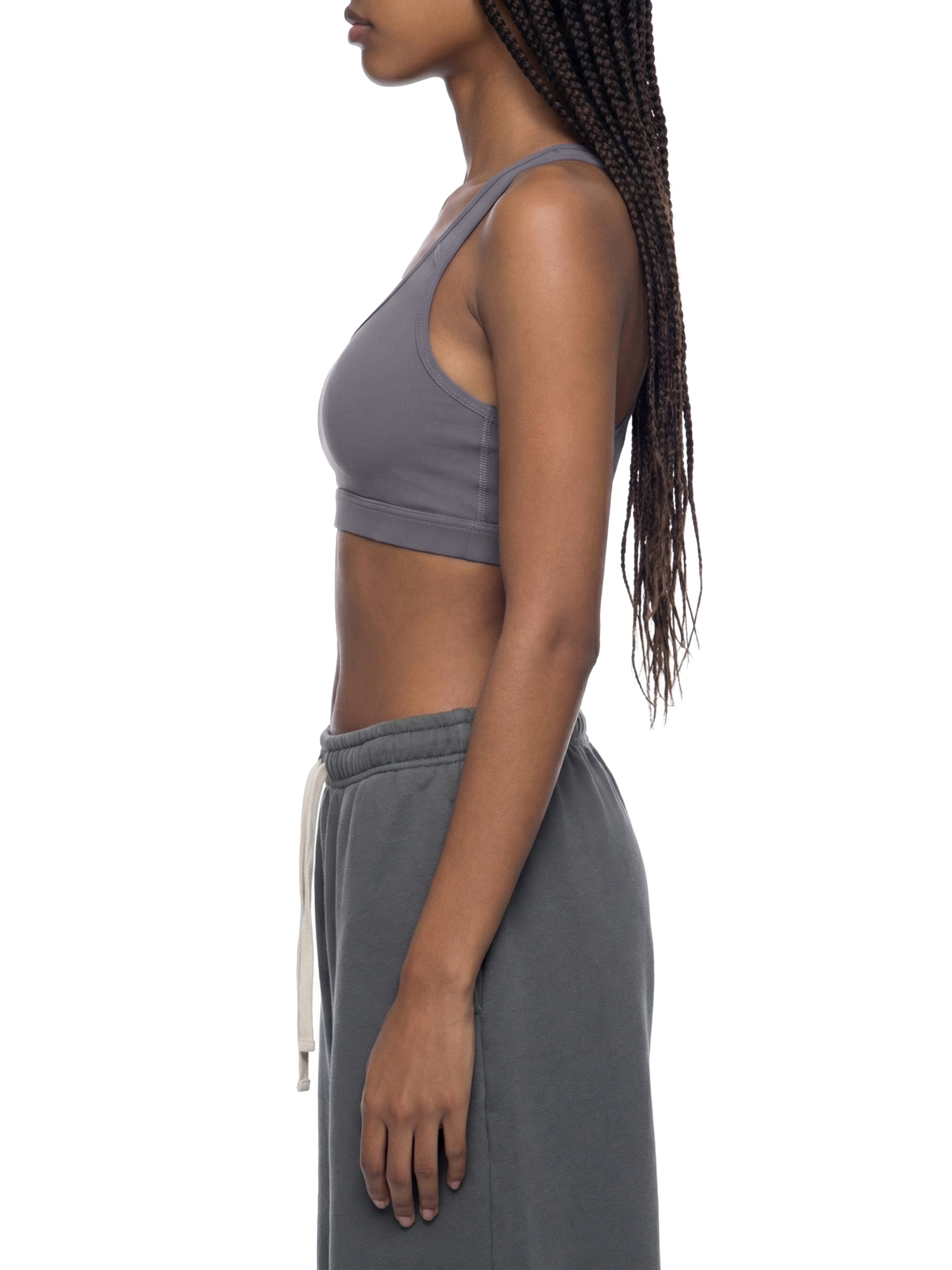Side view of woman in gray cropped sports bra and joggers, white background