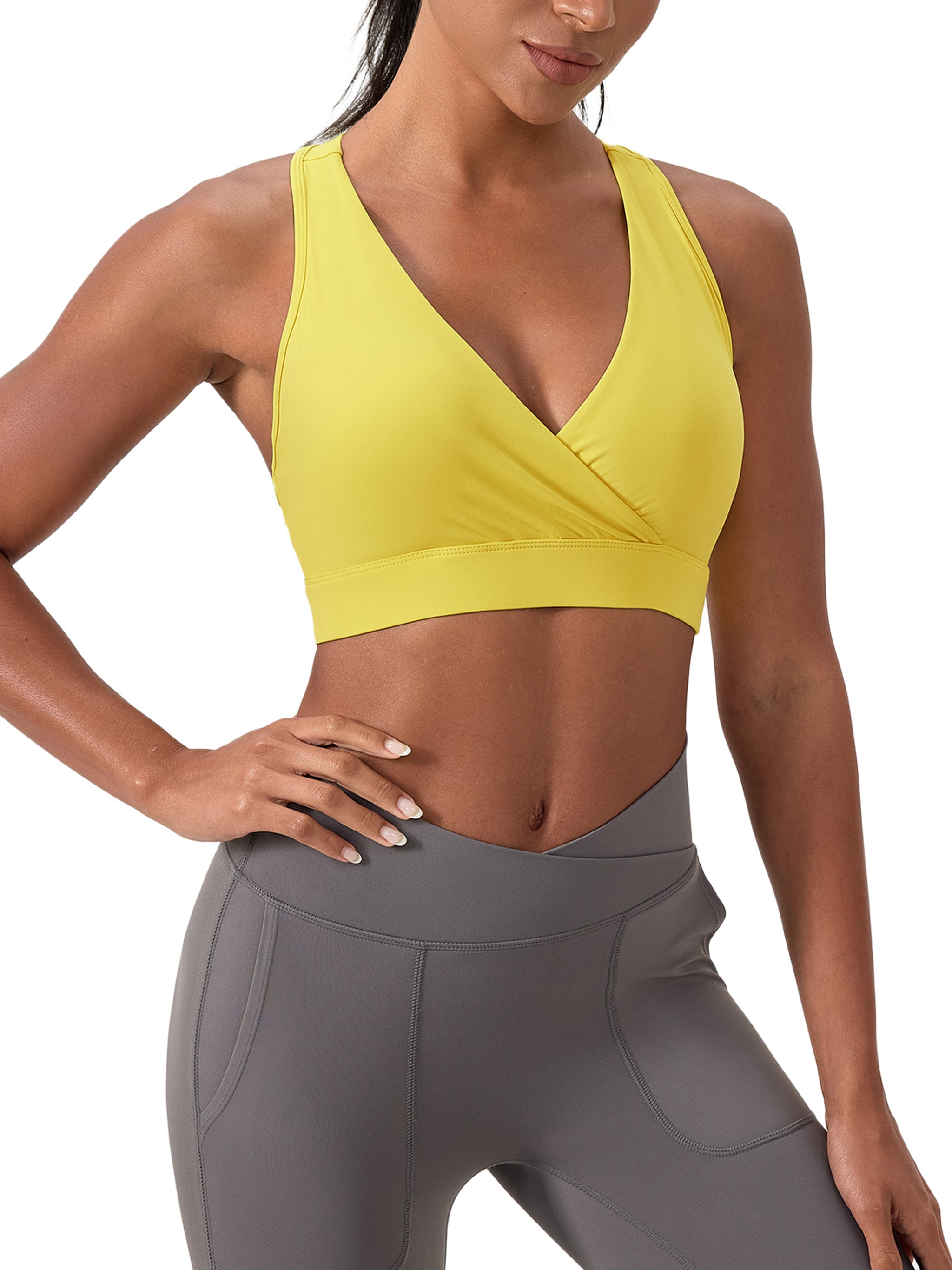 Woman wearing yellow crossover V-neck sports bra and gray high-waisted leggings