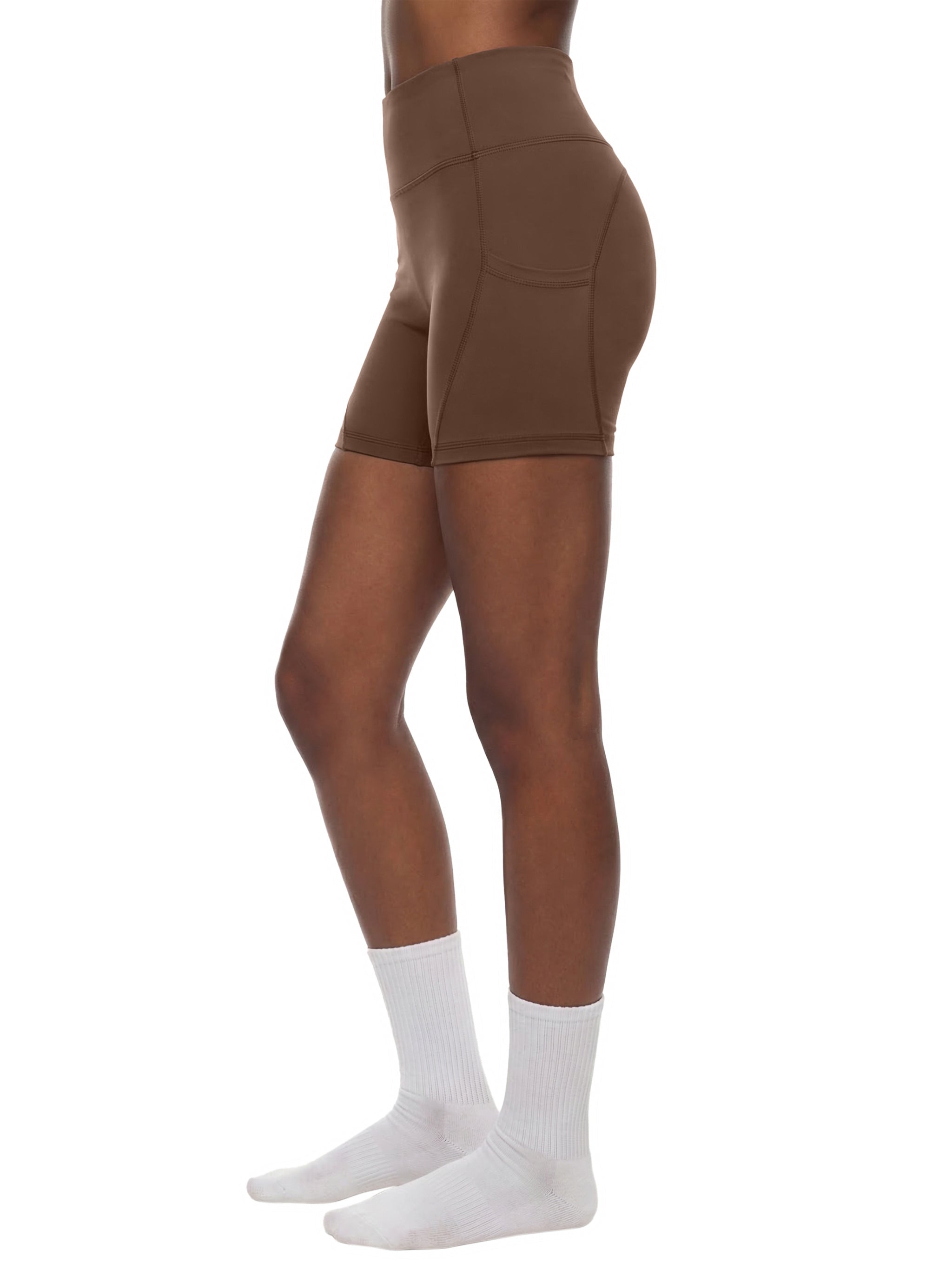 Woman wearing high-waisted brown biker shorts with pockets, standing in white socks