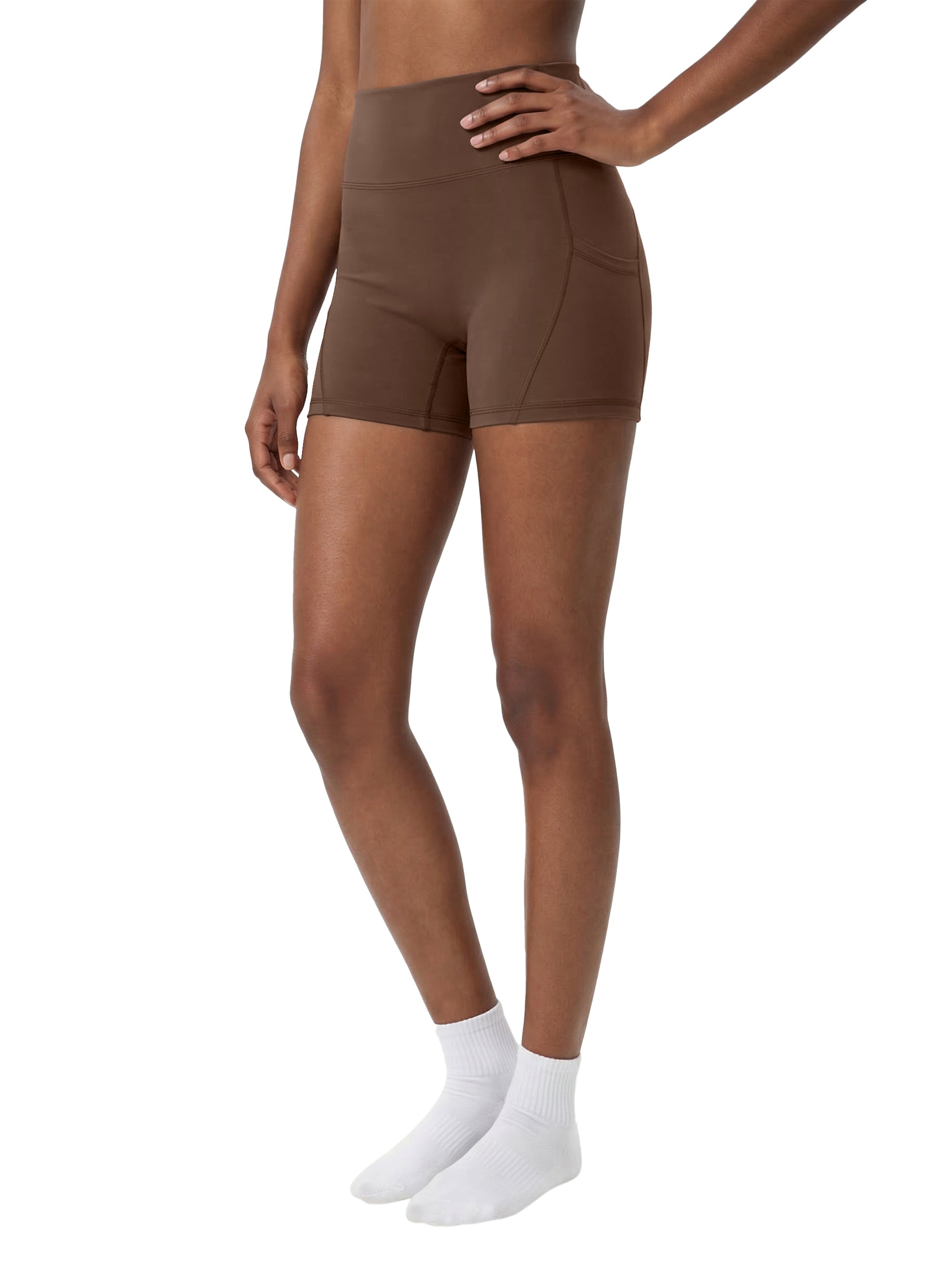 Woman wearing brown high-waisted biker shorts with side pockets, white socks, studio background