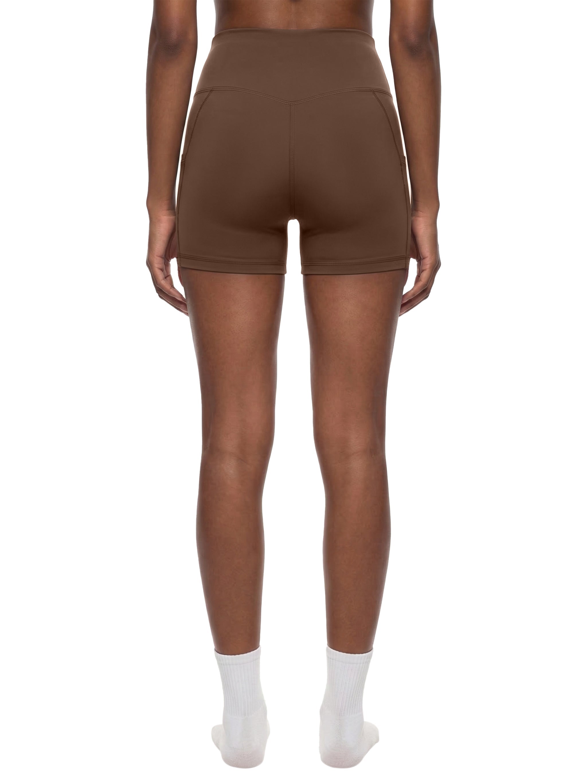 Back view of woman wearing high-waisted brown biker shorts with pockets on white background