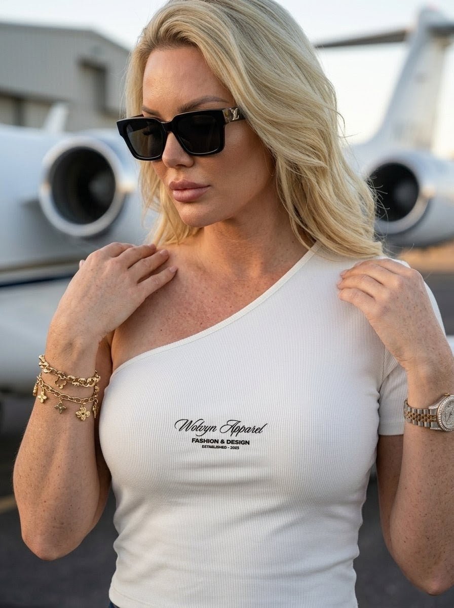 Woman in sunglasses wearing a white one-shoulder crop t-shirt near a private jet