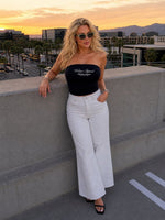 Woman wearing white vintage wash flared leg jeans and black tube top, rooftop at sunset