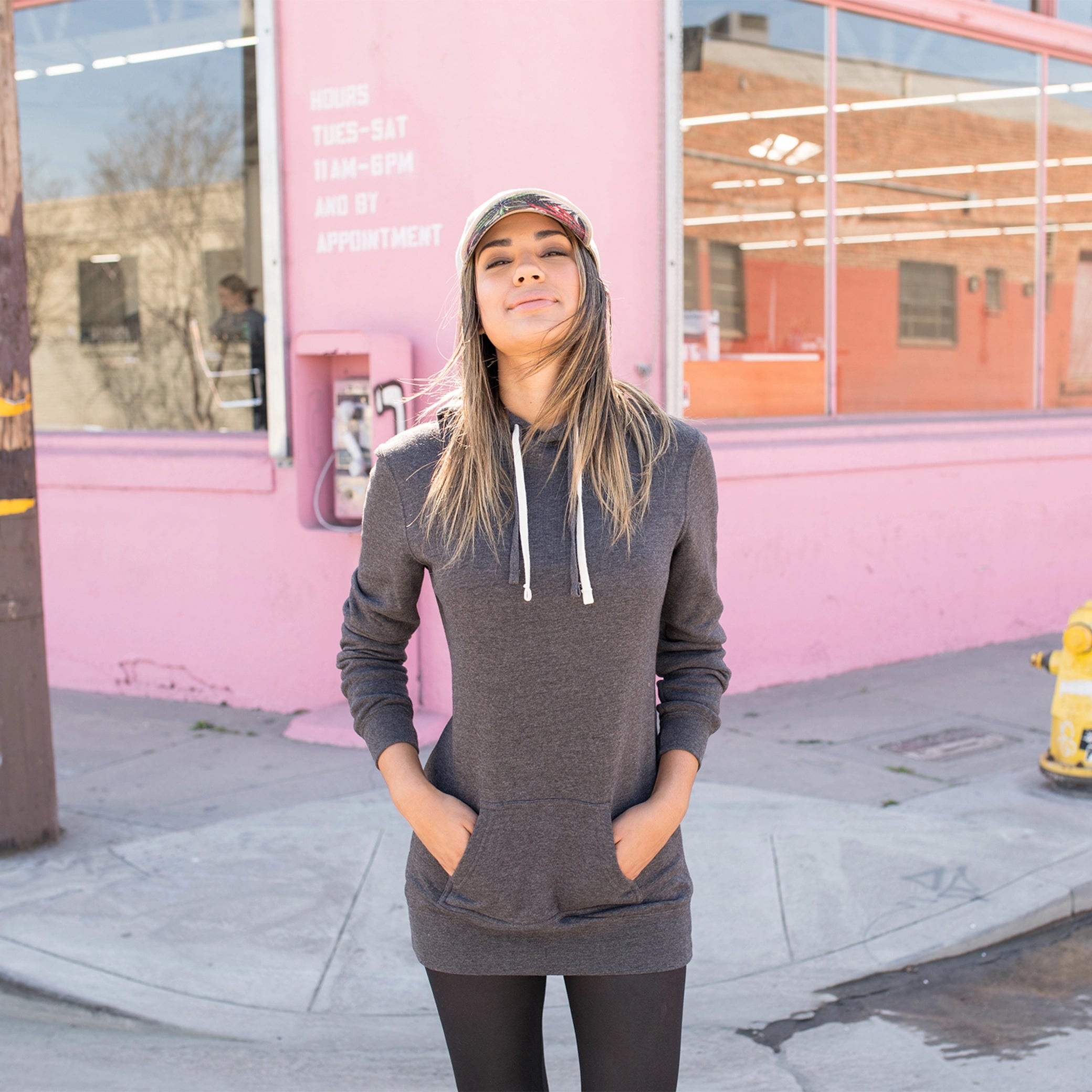 Woman in charcoal hooded sweatshirt dress posing outside a pink building in streetwear style