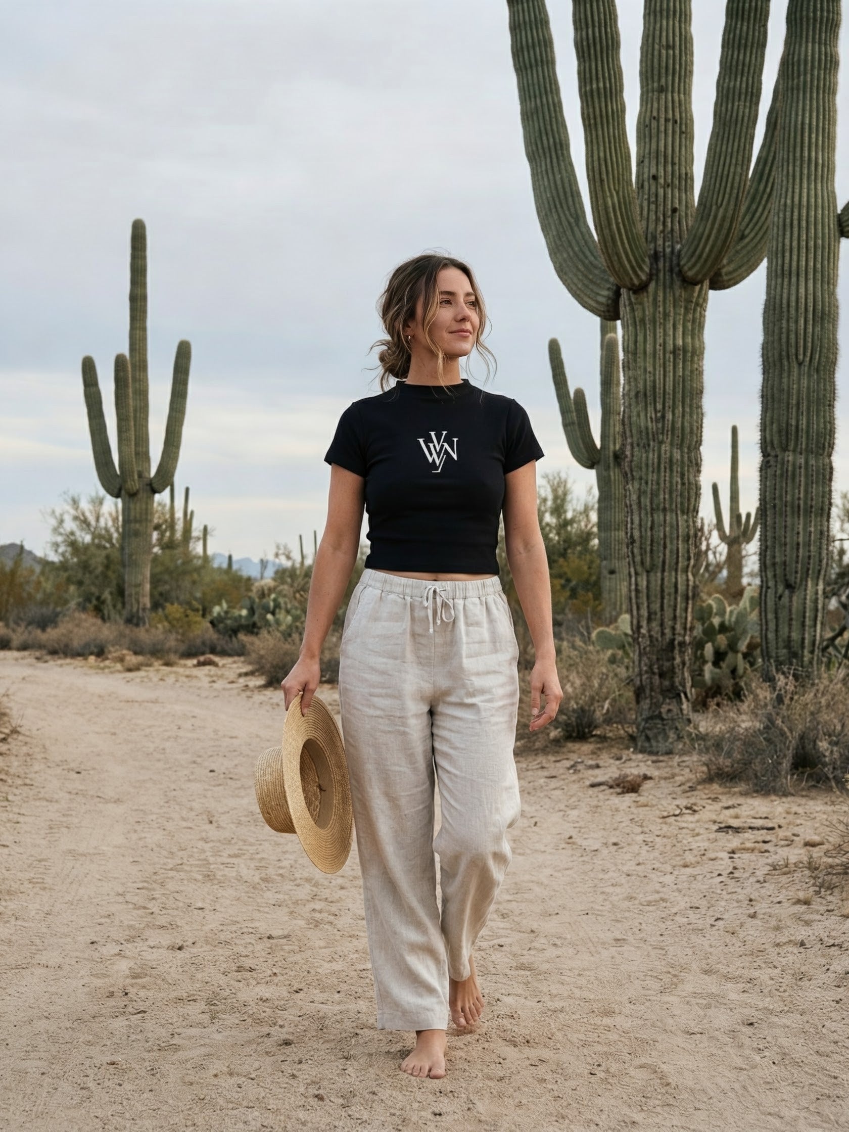 Woman in slim-fit black mock neck t-shirt and beige pants walking barefoot in desert with cacti