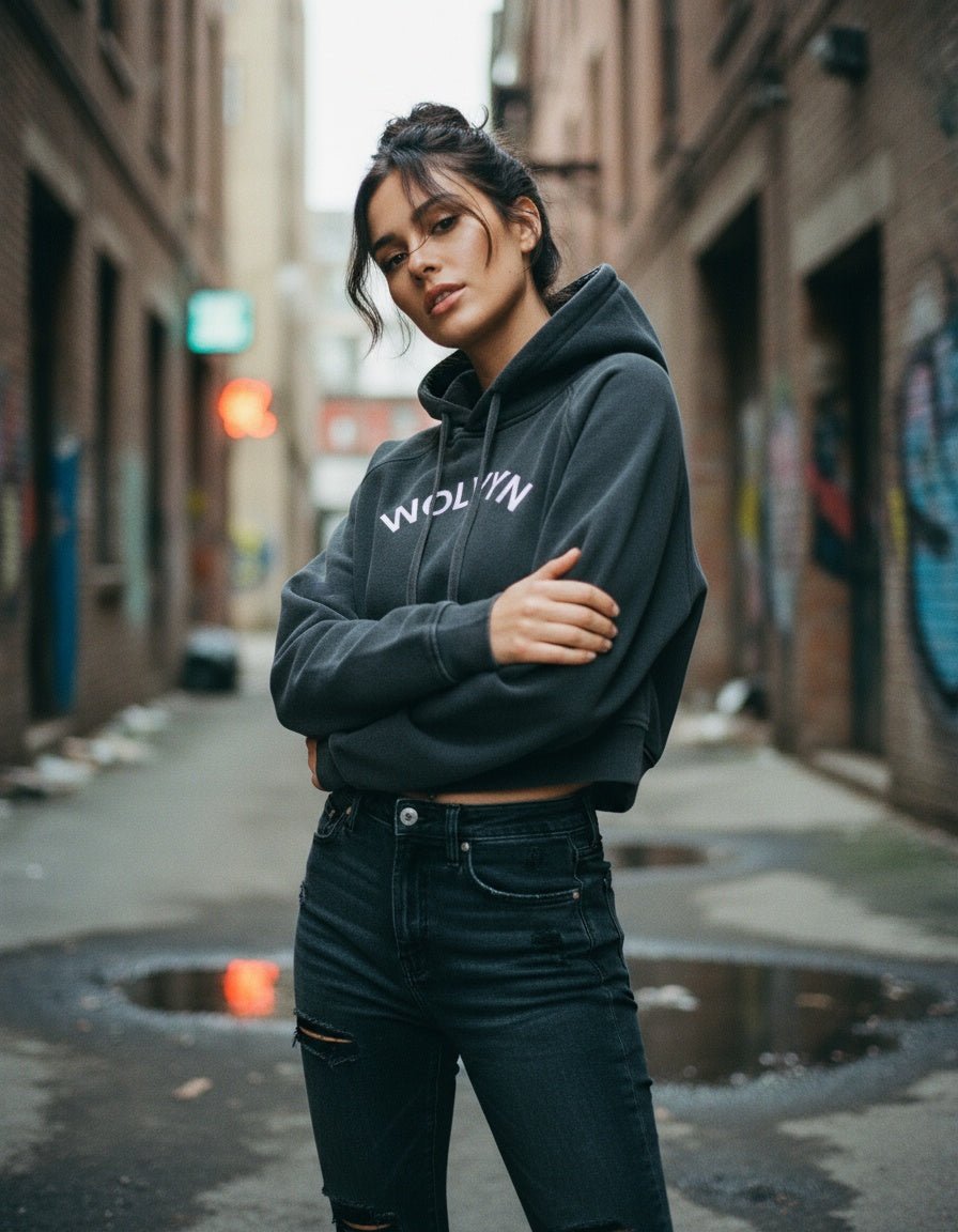 Woman in a snow-washed cropped hoodie and black jeans posing in an urban alley