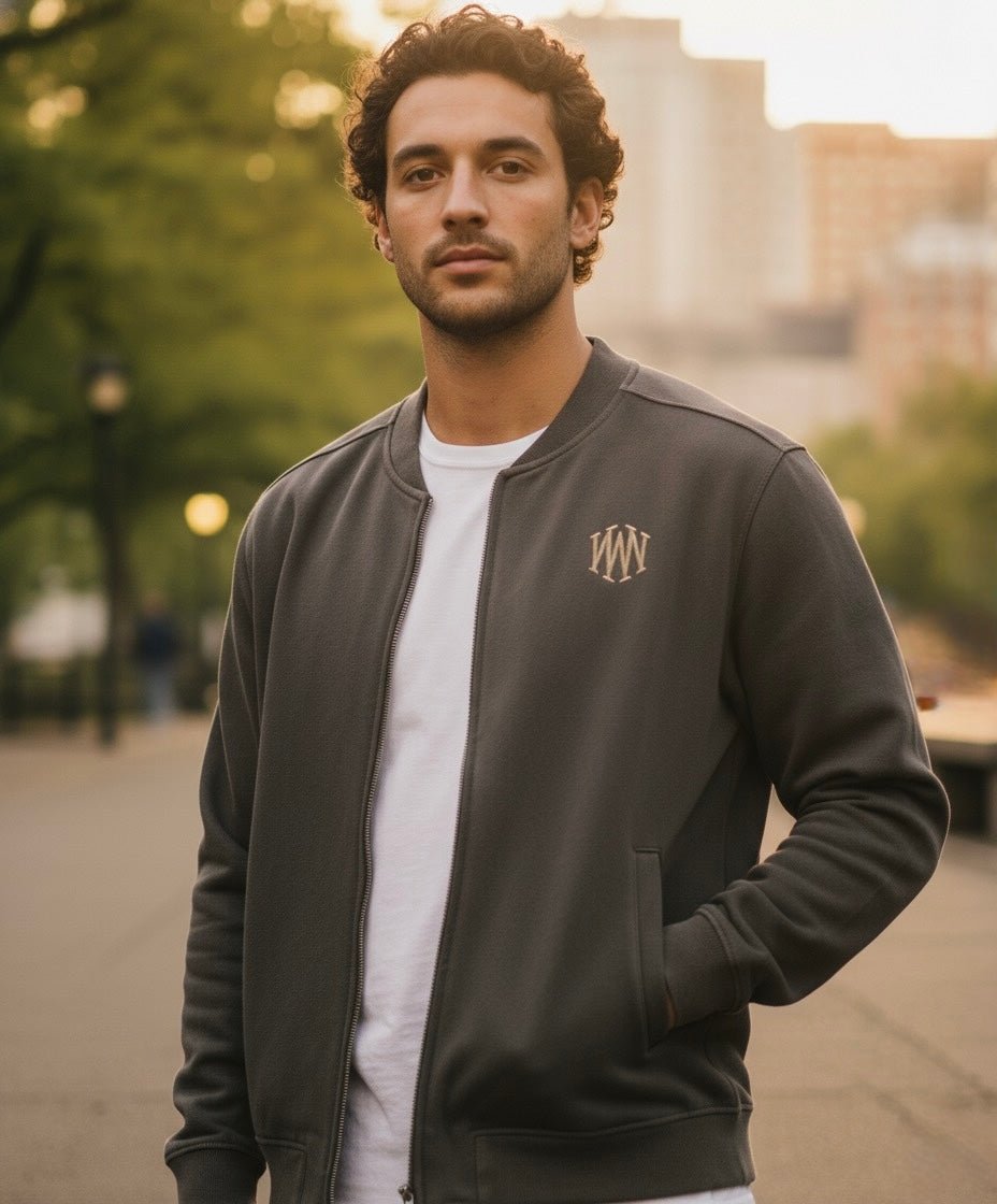 Man in heavyweight grey baseball jacket with white embroidered chest logo outdoors