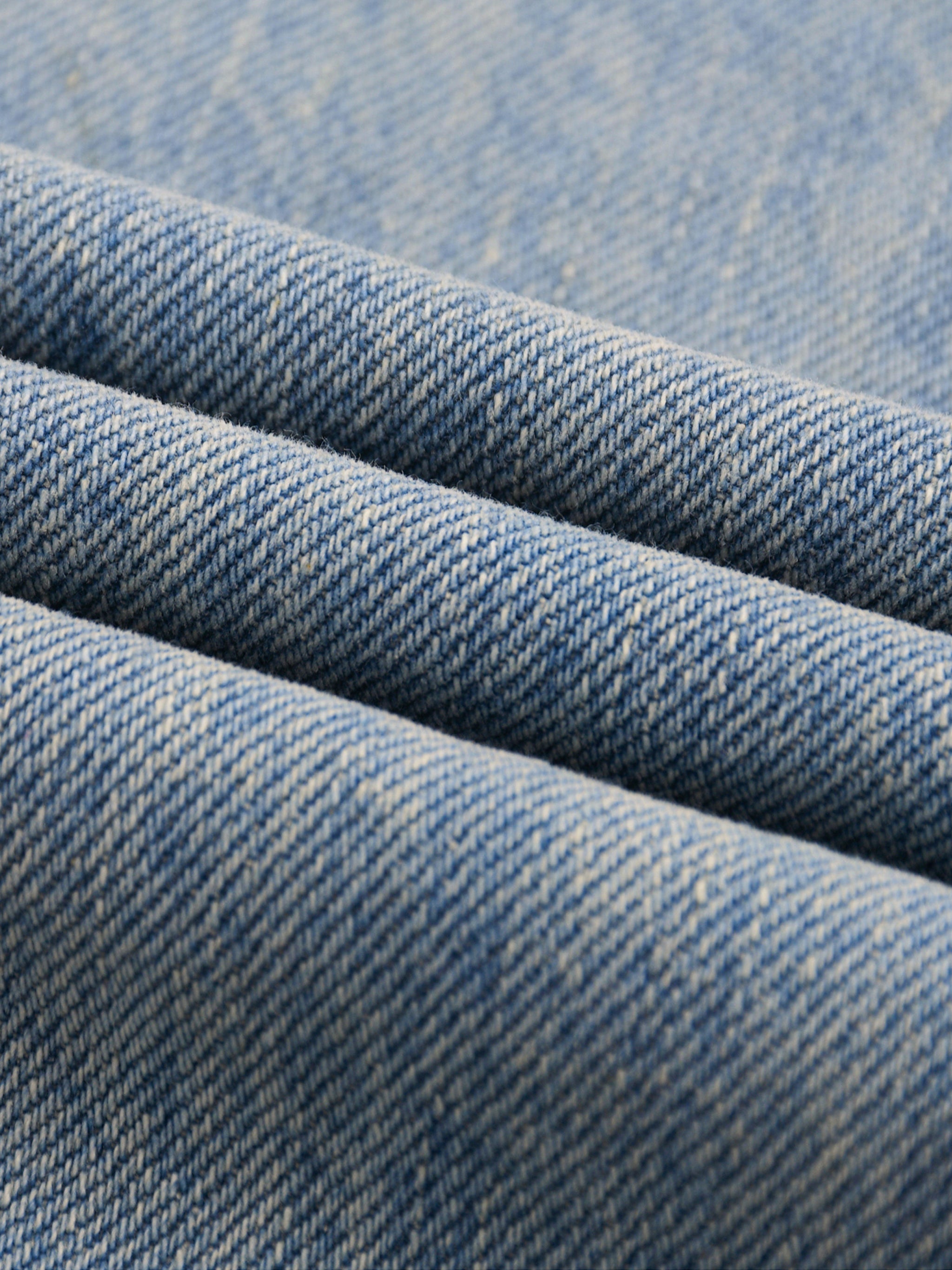Close-up of sun-faded light blue raw hem denim fabric texture